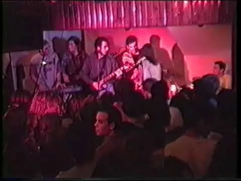 Banda tocando ante el público en un escenario pequeño iluminado en rojo